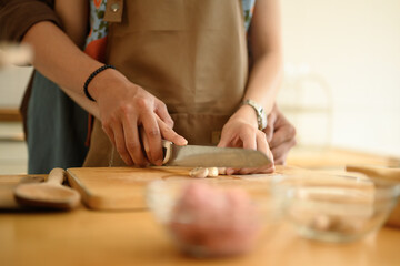 Woman in apron chopping garlic on wooden board, couple preparing food meal in the kitchen