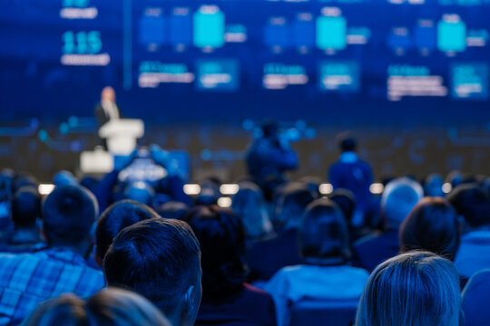 Professional conference with speaker presenting to an audience in a seminar hall, focus on crowd listening.