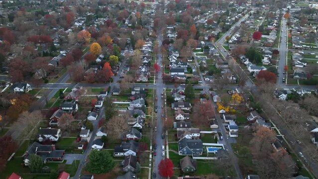Aerial shot of a suburban street with autumn-colored trees. High aerial reverse dolly shot above American neighborhood in fall at dusk.
