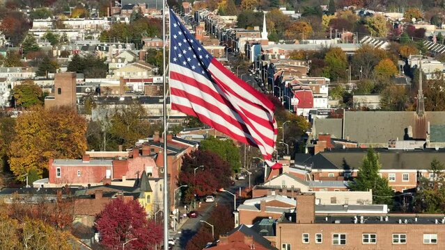 American flag waving in American city during autumn. Aerial rising shot with beautiful urban cityscape background.