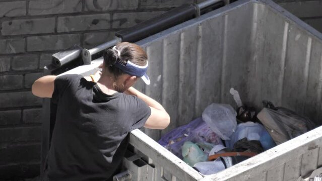 Hungry, poor, homeless woman rummaging through a trash can
