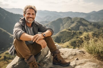 Handsome middle-aged man hiker sitting on top of a mountain and looking at the camera