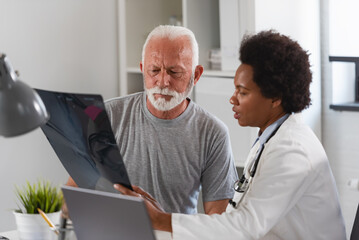 An African-American woman doctor specialist consults with an elderly male patient in her office
