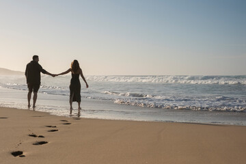 Pareja disfrutando el momento en la playa mientras se cogen de las manos. Momento tierno de amor - obrazy, fototapety, plakaty