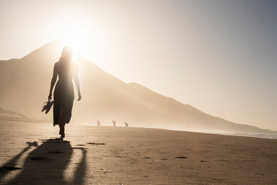 Silueta de una mujer joven disfrutando de una tranquila caminata al atardecer en la suave arena. Serenidad, naturaleza, puesta de sol, bienestar.