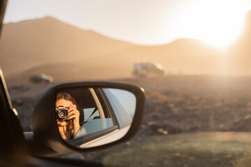 chica sacándose un retrato en el reflejo del espejo retrovisor del coche durante las vacaciones,...