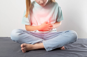 A little girl sits and holds her sore red stomach with her hands. Cognition of liver and...
