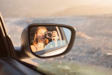 chica sacándose un retrato en el reflejo del espejo retrovisor del coche durante las vacaciones,...