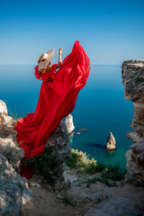 Red dress sea woman. Happy woman with flowing hair in a long flowing red dress stands on a rock...