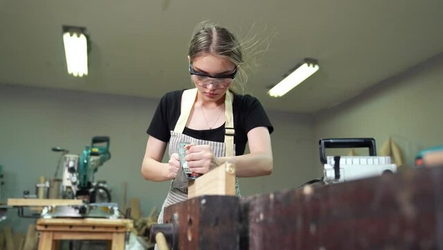 Hardworking woman carpenter using tools confidently in standing apron working in a craft workshop.