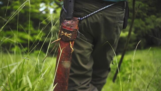 close up of male walking in a forest with machete big sharp knife and a wooden stick 