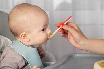 Feeding porridge and puree of a small child from a spoon. First meal. Copy space for text