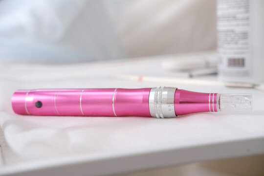 Professional Dermopen on a Sterile Table. A pink dermapen lies on a clean white table. Horizontal photo