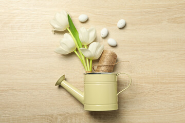 Tulips and twine in watering can, eggs on wooden background, top view