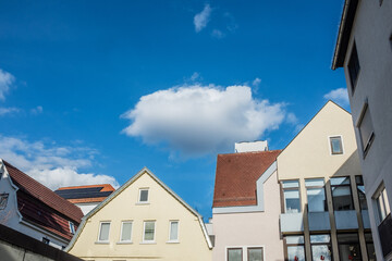 Sonnenbeschienene Giebel an Häuserzeile mit weißer Wolke vor blauem Himmel