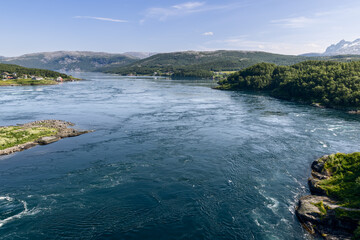 Fototapeta premium The dynamic Saltstraumen tide, captured from above, with its powerful whirlpools contrasting against the serene Nordic scenery and residential areas