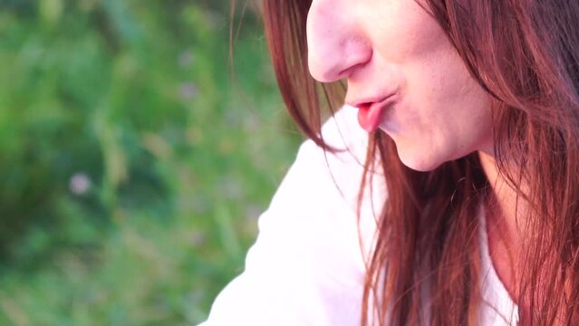 A happy young woman enjoys marzipan chocolate bar in nature at sunset, outdoor snack in the evening, admiring the summer sunset.