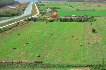 Fototapeta na wymiar Rural landscape with haystacks in the field and village in the background. Wonderful farmland in the spring. Green agricultural fields in Croatia