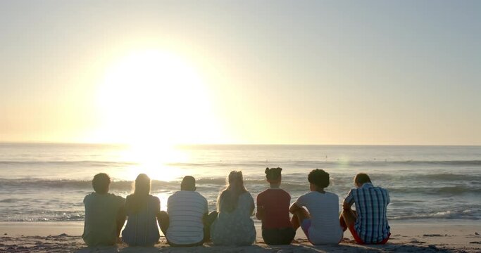 Diverse group of friends enjoy a serene beach sunset, with copy space