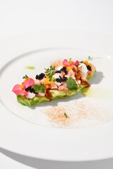 Gourmet avocado with shrimp tartare, mango, cream cheese, and black caviar on a pristine white plate