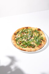 Italian pizza with cheese and mushrooms, adorned with arugula and cast in shadow on a white background