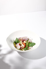 Greek salad with feta cheese, olives, and crisp vegetables, cast with shadows on a white background