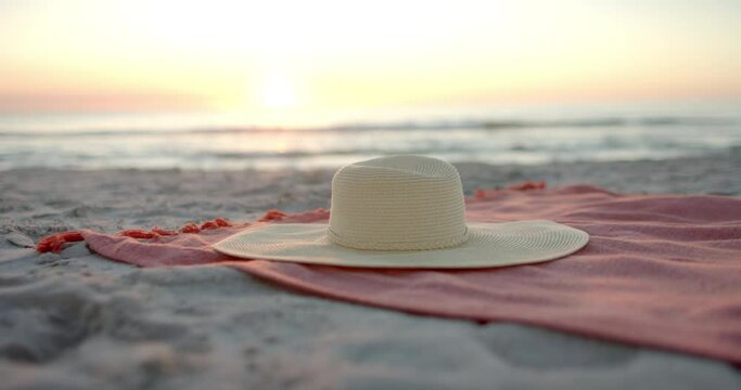 A diverse sun hat rests on a beach towel at sunset, with copy space