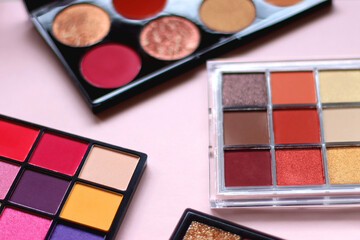 Various colorful eyeshadow palettes on bright pink background. Selective focus.