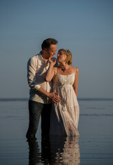 beautiful  happy couple, bride and groom in white dresses walking in the ocean on sunny summer day and holding each other hand by hands