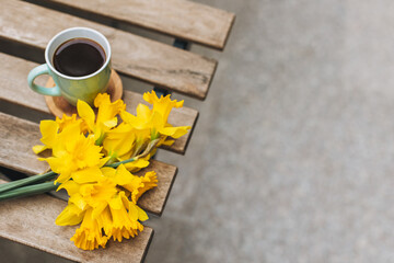 Cup of black coffee and bouquet of yellow daffodils (narcissus) on a wooden table in a street cafe.