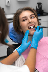 Close-up of a dentist examining a patient's teeth in the dentist's office. Young beautiful woman at a dentist appointment. Concept of oral care. Vertical photo