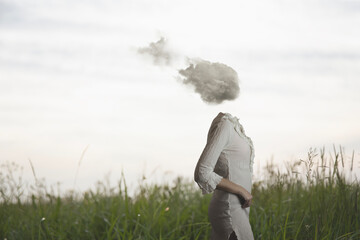 surreal woman with a cloud on her head walking freely and lightly in a meadow - 741351675