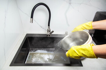 Man's hands in yellow gloves pour pots of hot water into a sink with dirty filters from the hood in...
