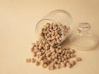 Extruded wheat bran is poured out of a glass jar onto a beige background, next to it lies a lid, an empty place for text. The concept of proper snacking, nutrition and weight loss