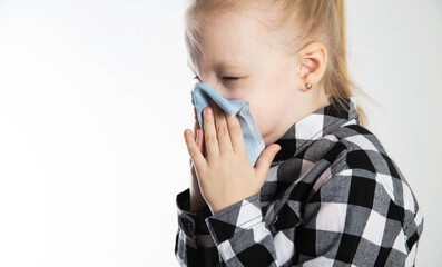 A girl aged seven years old in a checkered shirt blows her nose into a handkerchief on a white...