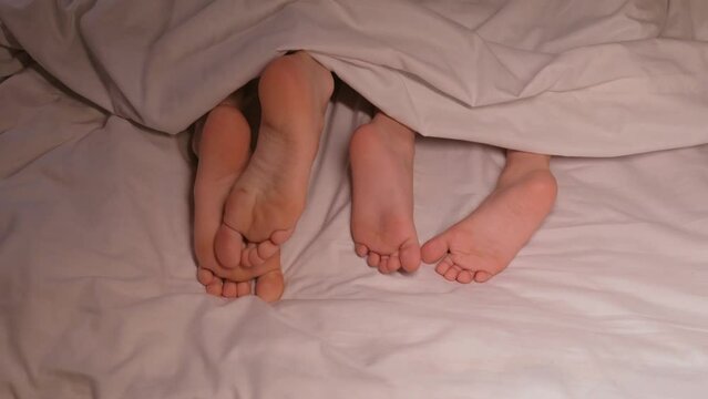 restless feet of the boy son kid and mother female legs scabies and itch under blanket on sheet at night. Mom woman and child girl daughter scratch bare feet with fungus from itching in bed