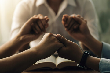 Group of people holding hands praying worship believe with light from the window. the Holy Bible. They were reading the Bible and sharing the gospel. Christians and Bible study concept.