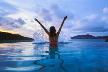 Asian traveler bikini woman relax and travel in infinity pool resort at sunset in phuket beach...