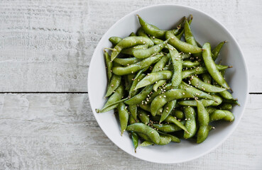 Edamame salted green soybeans in bowl on white wooden table with space for text. Top view.
