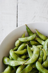 Edamame salted green soybeans in bowl on white wooden table with space for text. Top view.

