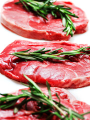 Three uncooked boneless lamb leg steak with fresh rosemary herb on white background. Premium high quality meat product of agriculture industry. Butcher craft and skill. Food supply chain.