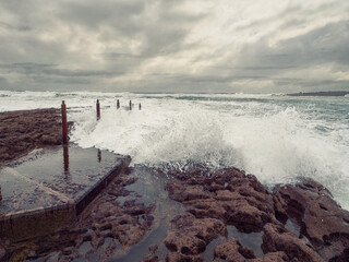 Wave hits footpath to the ocean creating splash of water. Dramatic nature scene. Low angle of view....