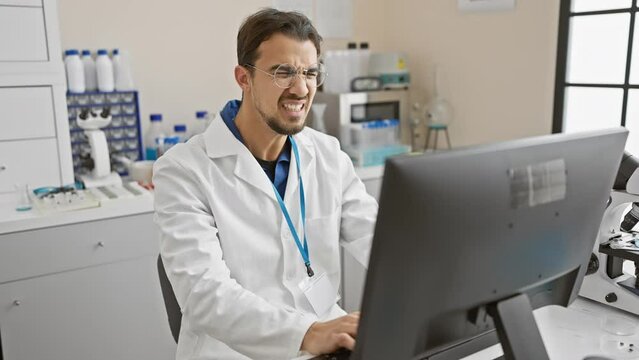 A young hispanic man with a beard works attentively in a laboratory indoors, analyzing data on a computer