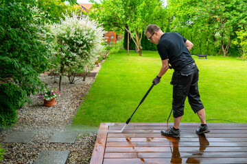 man cleaning terrace with a power washer - high water pressure cleaner on wooden terrace surface - 741374411