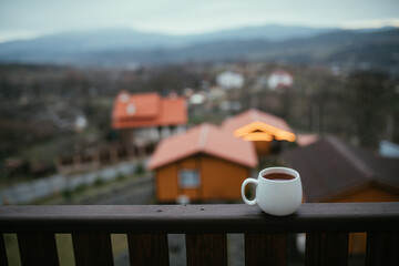 White cup with hot tea on wooden balcony with mountains view.