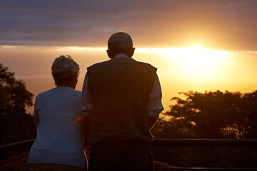 Senior couple, sunset and view on balcony in outdoors, bonding and love on vacation or holiday. Back, elderly people and dusk on terrace and together in nature, security and travel for marriage