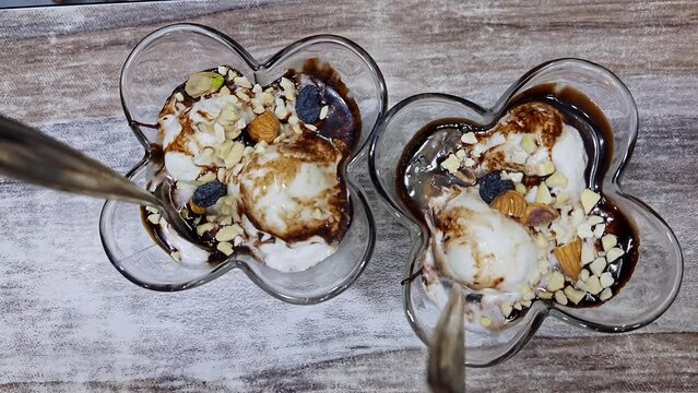 Vanilla ice cream with chocolate sauce and crushed nuts served in a glass bowl