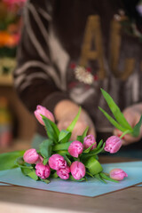 Close-up of a florist collecting a bouquet of pink tulips on a table, selective focus. Vertical photo