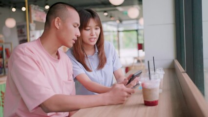 Two young male and female friends chatting and looking at smartphones in a coffee and burger shop.Happy lifestyle day