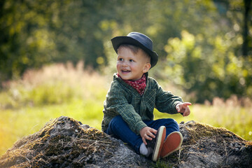 Cute Little Happy Boy with Hat Sitting in Summer Forest - 741386683